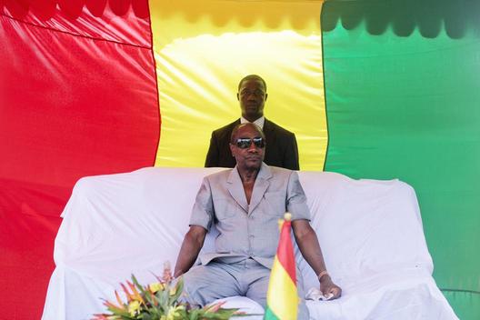 Телохранитель стоит за спиной президента Гвинеи Альфа Конде перед выступлением на публичном мероприятии в одном из районов города Конакри (столица Гвинеи). 19 апреля 2013 год.